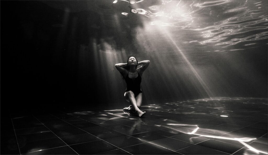 Black and white underwater shot of a woman in a peaceful pose, capturing light play.